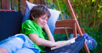 Smiling boy while lying on the swing and reading a book