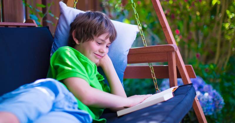 Smiling boy while lying on the swing and reading a book