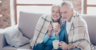 A lovely retire couples sharing one blanket holding both a mug with coffee